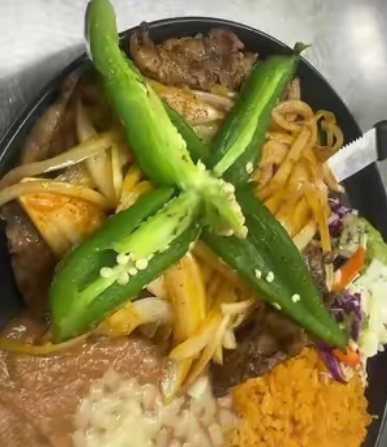 A sizzling fajita plate with grilled peppers, onions, rice and beans